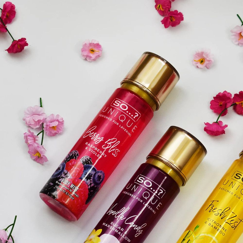 Drei Körperspray-Flaschen mit goldenen Deckeln. Aufschrift: So Unique. Produkte: Berry Bliss, Vanilla Candy, Fresh Zest. Umgeben von Blüten.