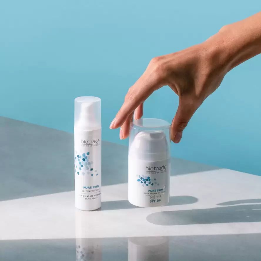 Zwei weiße Creme-Flaschen. Eine wird von einer Hand gehalten. Aufschrift: Biotrade, Pure Skin Glow Revival Day Cream SPF 50+.