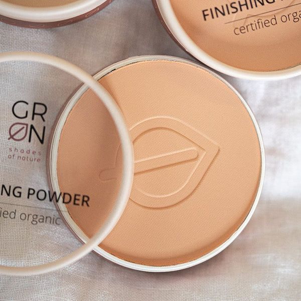 Beige Puderdose mit Deckel. Aufschrift: GRÜN, Finishing Powder, certified organic. Blatt-Logo.