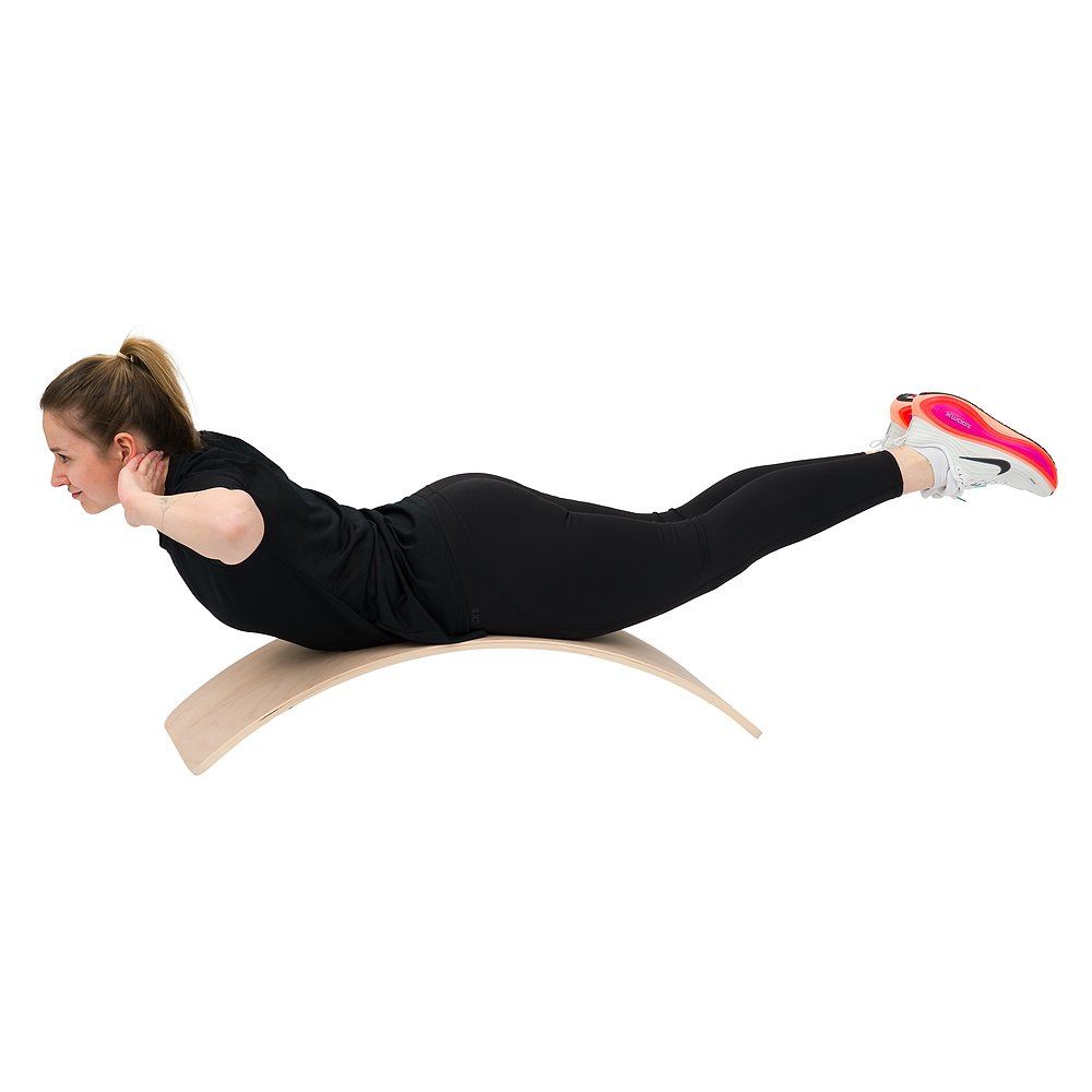 Frau in Bauchlage auf einem Balance Board, Beine gestreckt, Hände hinter dem Kopf.