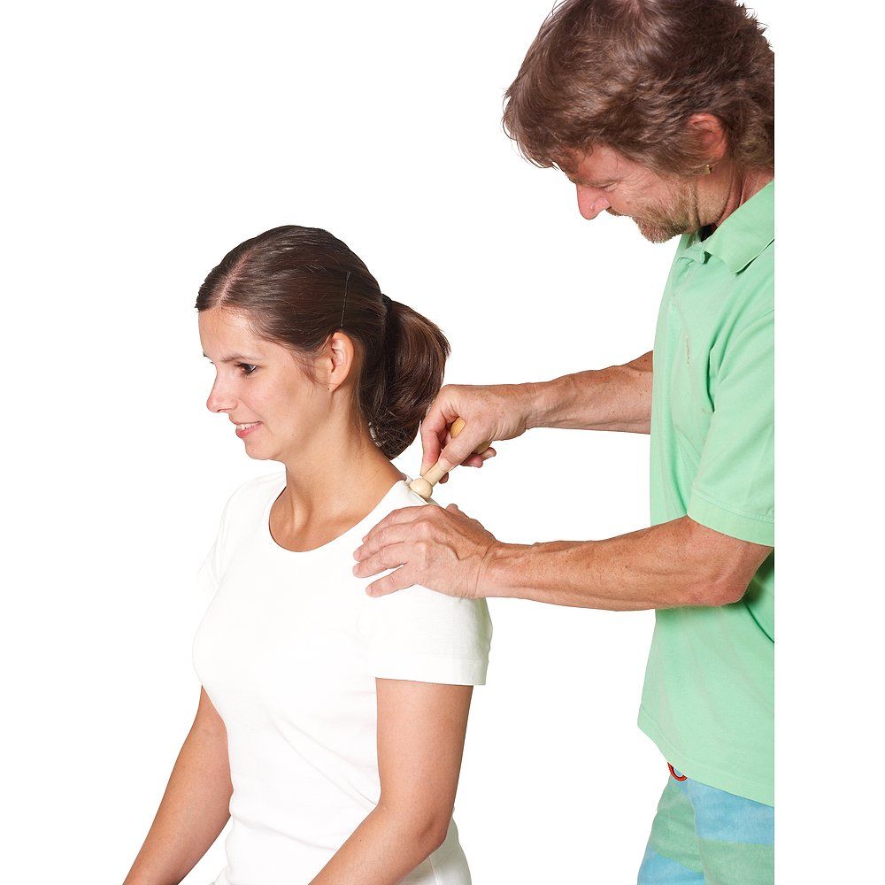 Person massiert Schulter einer anderen Person mit einem Holzstab. Helle Haut, helle Kleidung.