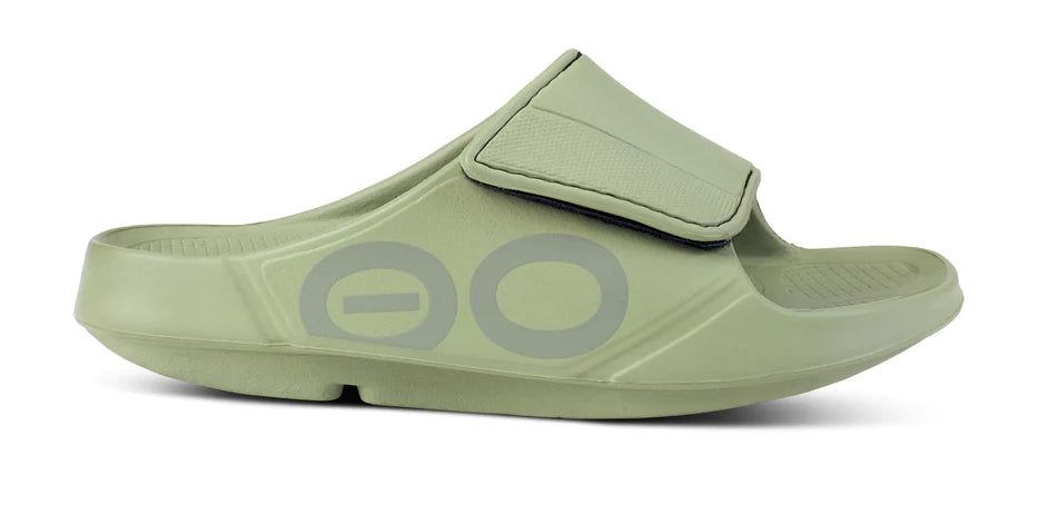 Hellgrüne Sandale mit verstellbarem Riemen. Seitlich ist das Logo "OO" zu sehen. Die Sohle ist leicht gewölbt.