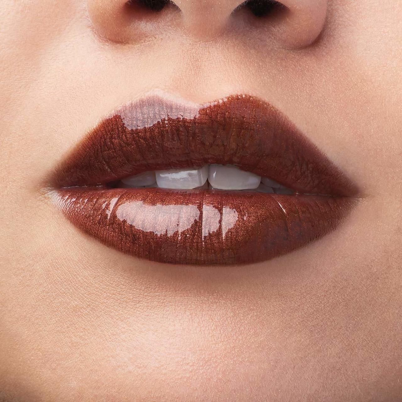 Nahaufnahme von Lippen mit braunem Lip Lacquer. Glänzendes Finish. Deutlich sichtbare Lippenkonturen und Zähne.