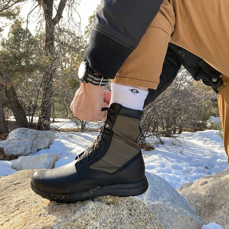 Person bindet Schnürsenkel. Weiße Kompressionssocken und Stiefel. Im Freien.