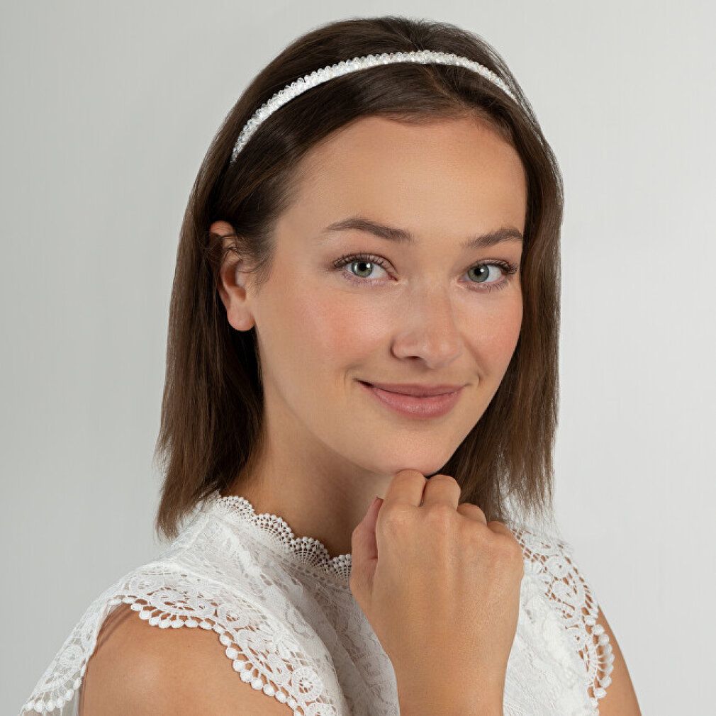 Frau mit weißem Stirnband mit weißen Verzierungen. Sie trägt ein weißes Oberteil.