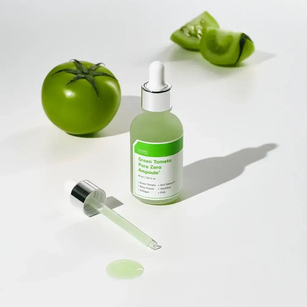 Grüne Flasche mit Pipette und grüner Flüssigkeit. Daneben eine grüne Tomate und Tomatenscheiben. Aufschrift: Green Tomato Pore Zero Ampoule+.