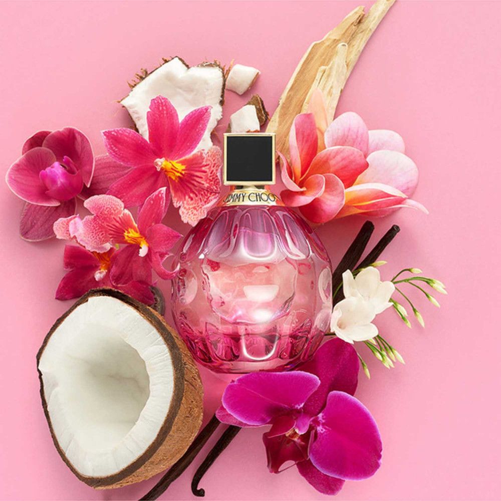 Rosa Jimmy Choo Rose Passion Flakon, umgeben von Blüten, Kokosnuss und Vanilleschoten. Flakon rund, rosa, mit schwarzem Deckel.