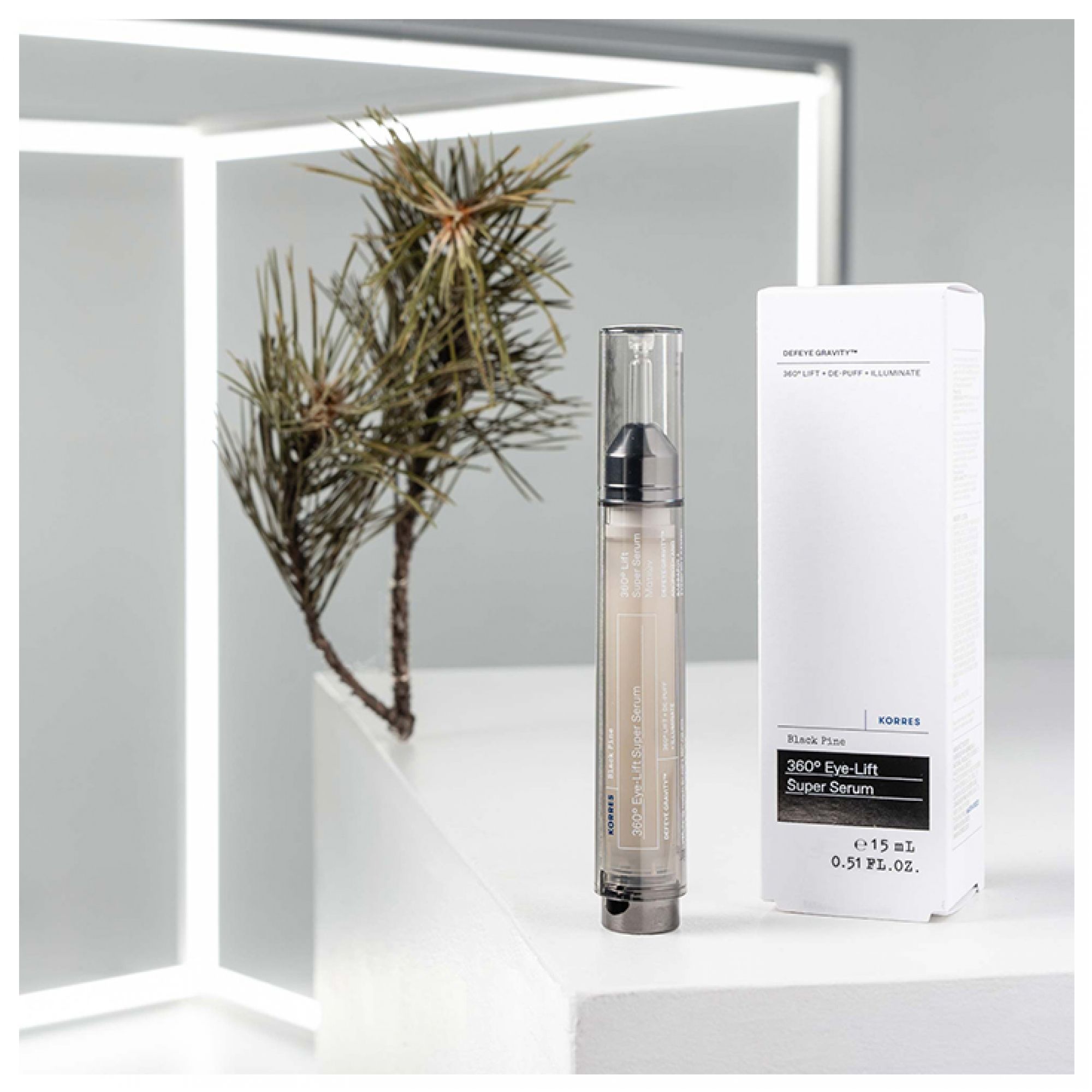 Ein transparenter Flakon mit schwarzem Applikator neben einer weißen Produktbox. Ein Zweig mit Nadeln ist im Hintergrund.
