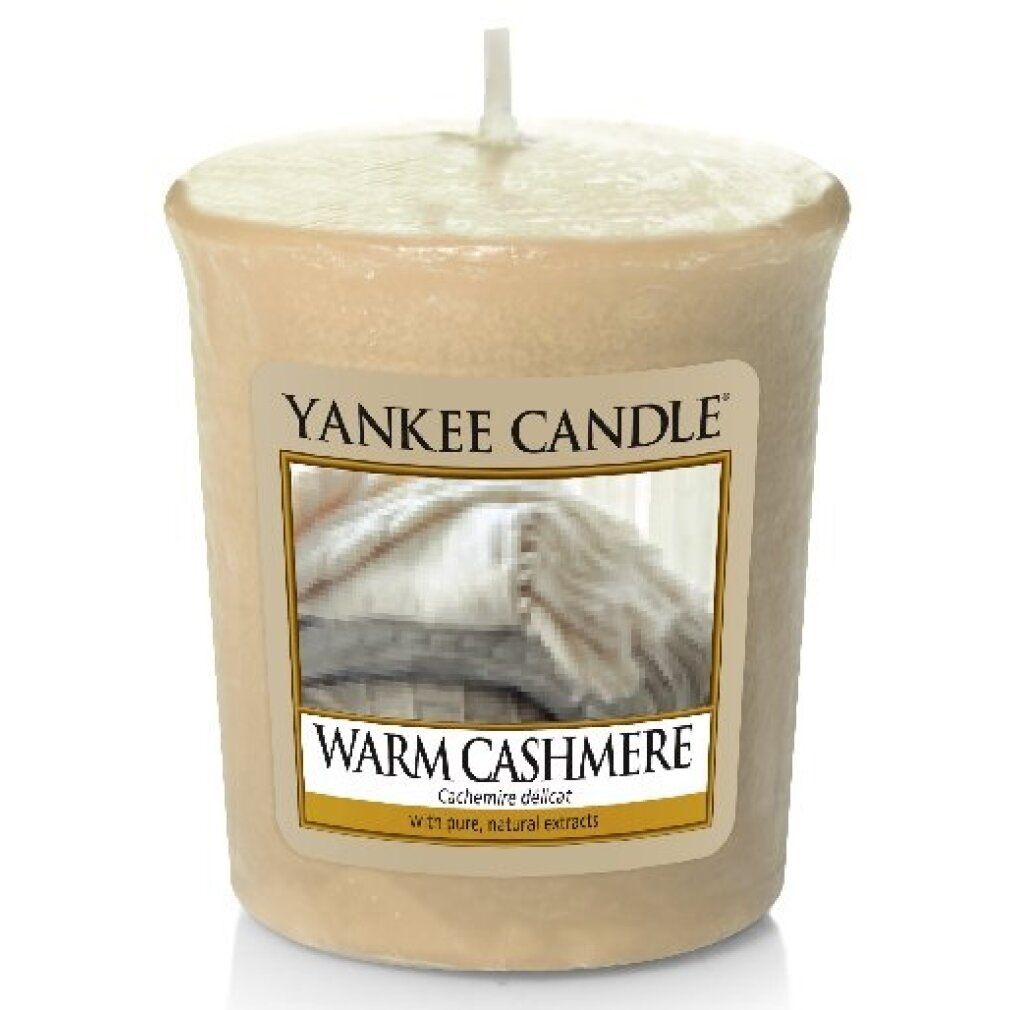 Beige Duftkerze mit Etikett. Aufschrift: Yankee Candle, Warm Cashmere. Abbildung von Decken. Mit Docht.