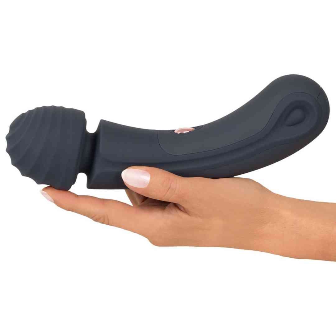 Dunkelgrauer Massage-Wand, gehalten in einer Hand. Geriffelte Spitze, geschwungener Griff. Rosa Knopf.