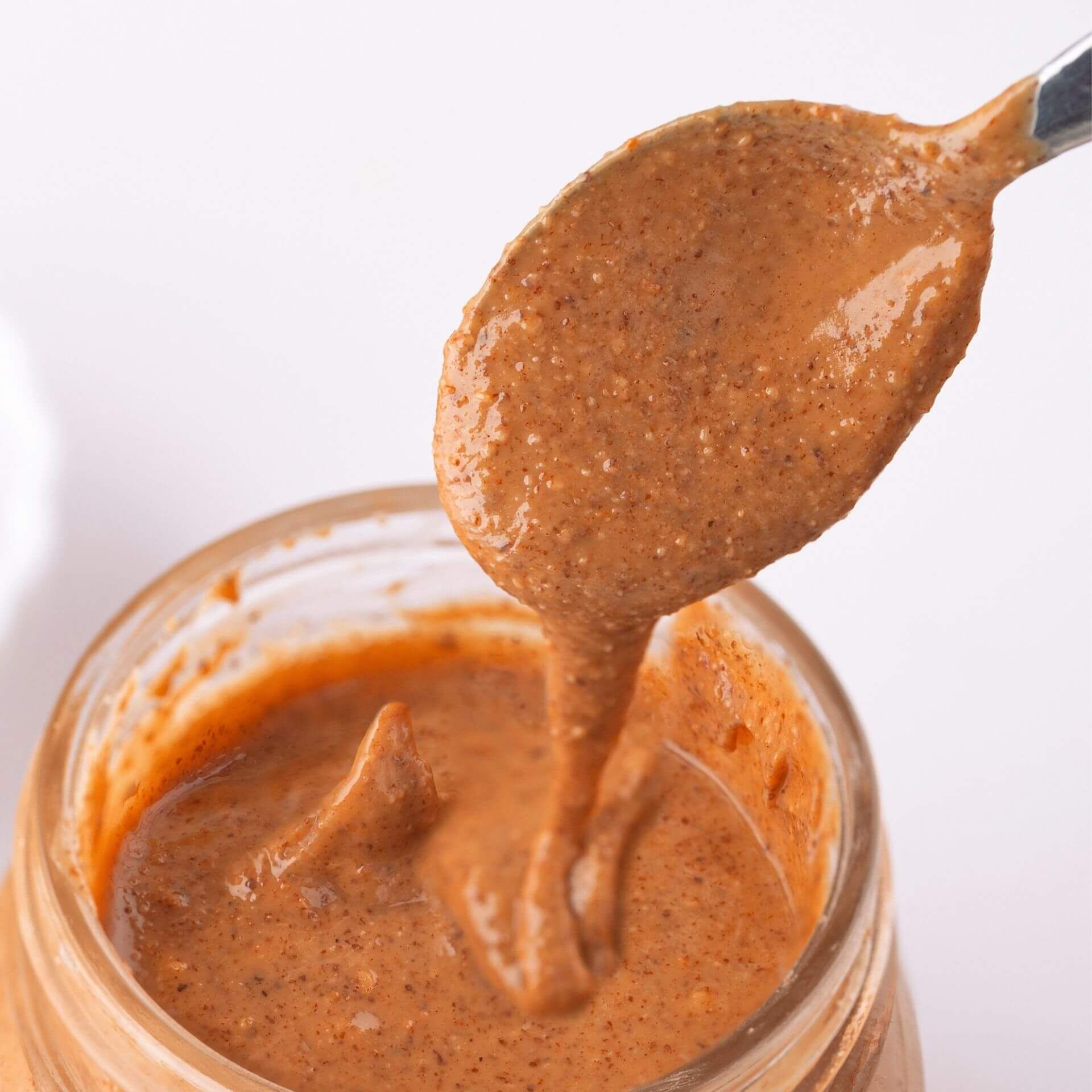 Glas mit Haselnussmus, Löffel mit cremiger Paste. Nahaufnahme, helle Umgebung.