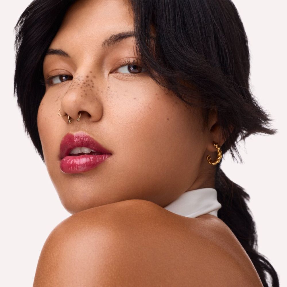 Porträt einer Frau mit Lippenfiller Gloss. Dunkle Haare, Nasenpiercing, goldene Ohrringe.