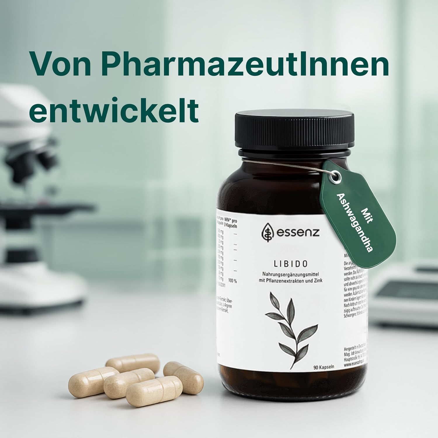 Braune Flasche ESSENZ Libido Kapseln, grüne Anhänger. Kapseln daneben. Hintergrund: Labor. Text: Von Pharmazeutinnen entwickelt, Mit Ashwagandha.