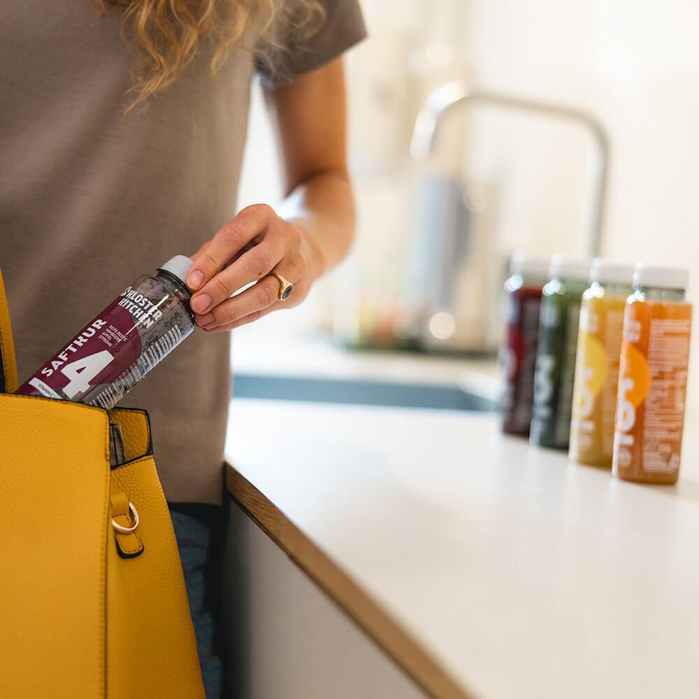 Eine Person hält eine Flasche Kloster Kitchen Saftkur, Nummer 4, in einer gelben Tasche. Im Hintergrund weitere Flaschen.