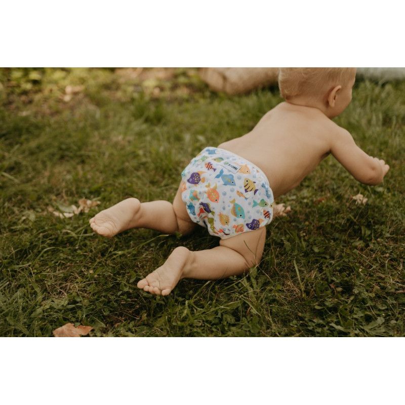 Baby krabbelt auf Gras. Schwimmwindel mit Meeresmotiven. Bunte Fische und Seesterne. Kind von hinten gesehen.