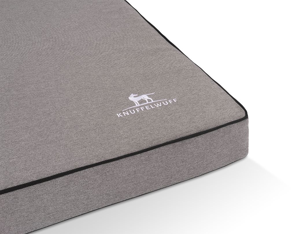Detailansicht der orthopädischen Hundematte. Graues Material, schwarzer Rand. Knuffelwuff-Logo. Auf weißem Hintergrund.