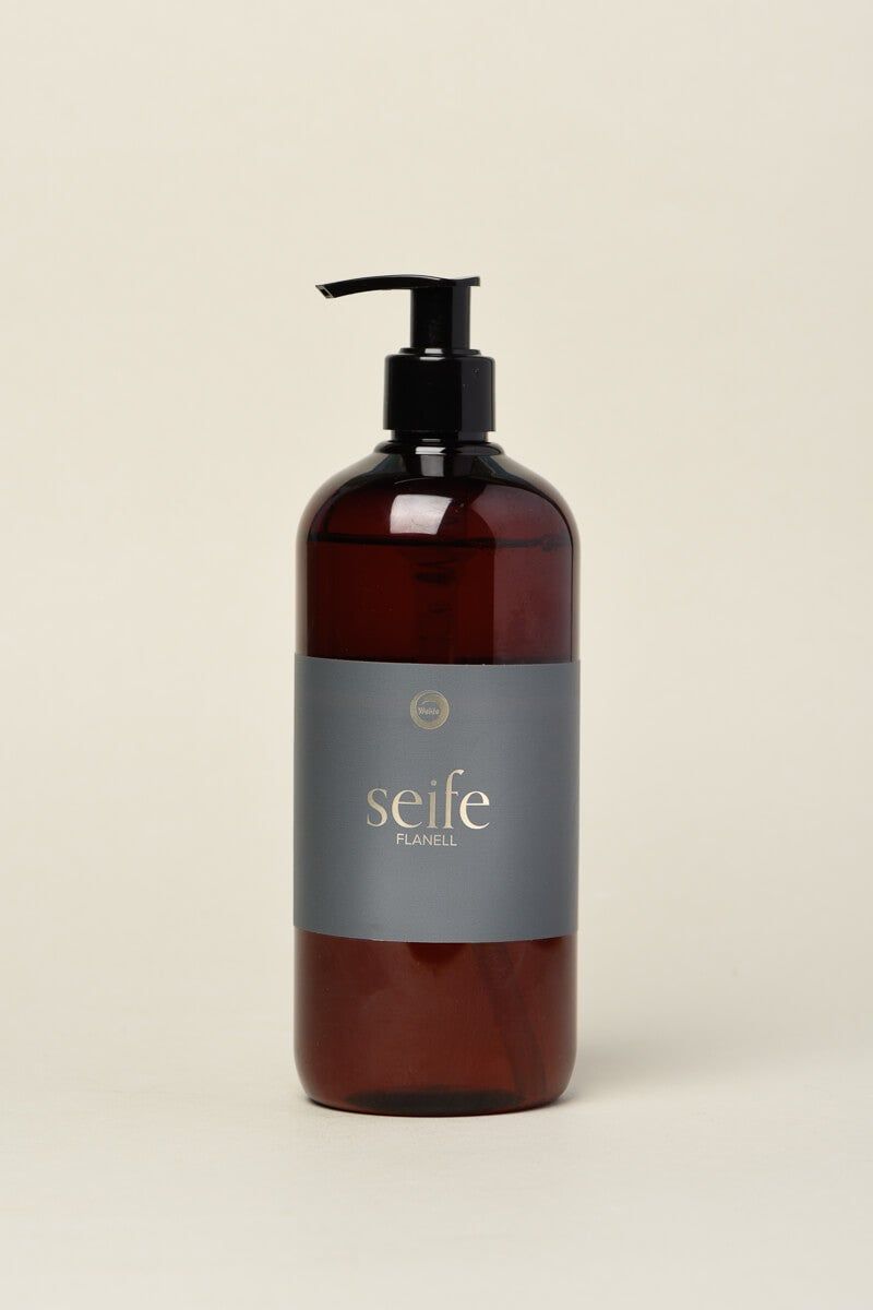 Braune Flüssigseife in einer Flasche mit schwarzem Spender. Auf dem Etikett steht "seife" und "Flanell".