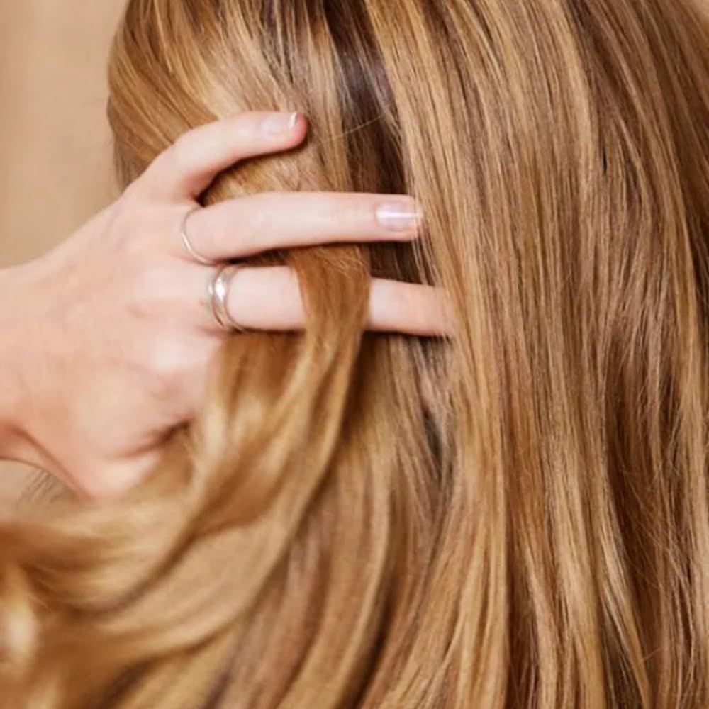 Helle Haarsträhnen, die von einer Hand gehalten werden. Die Hand trägt Ringe. Das Haar ist glatt und glänzend.