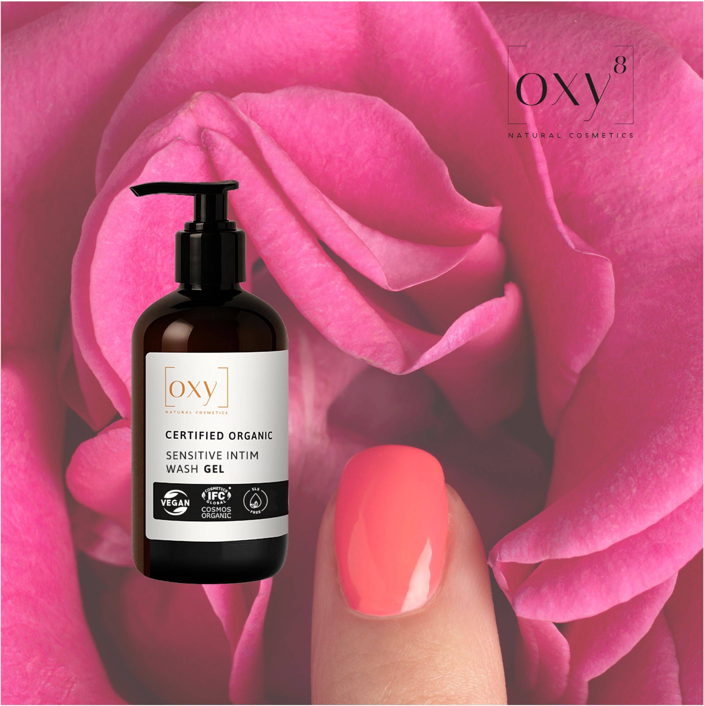 Braune Flasche mit Pumpe vor rosa Rosen. Aufschrift: SENSITIVE INTIM WASH GEL. Logos: Vegan, IFC Cosmos Organic. Nagel mit Nagellack.
