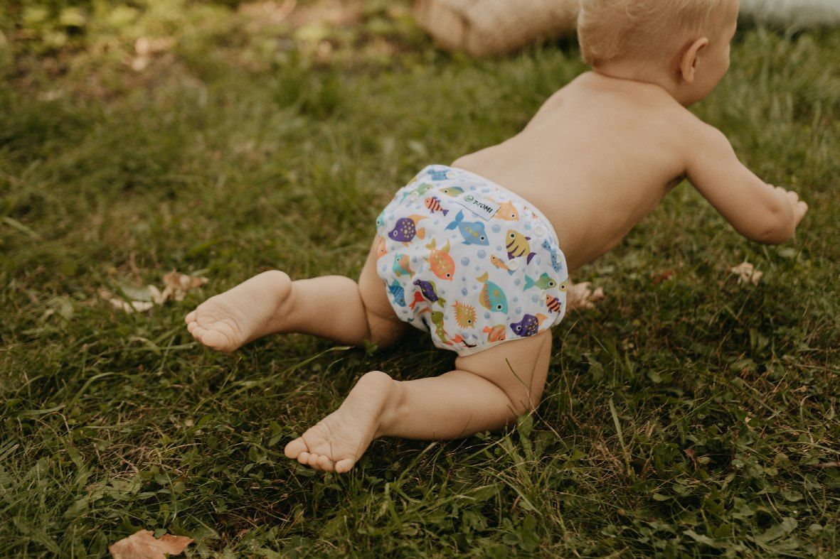 Baby krabbelt auf einer Wiese. Es trägt eine T-TOMI Schwimmwindel mit Fischmuster.