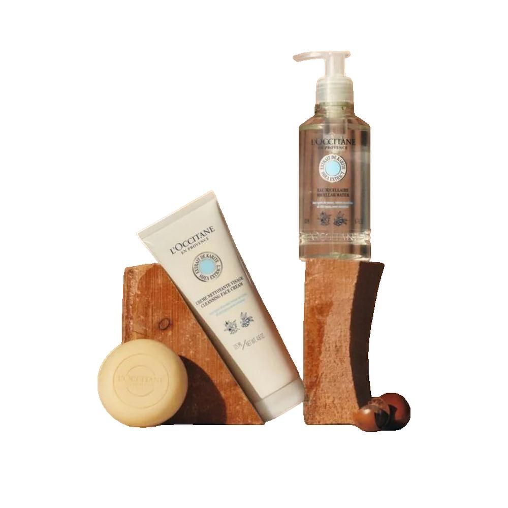 Drei L'Occitane-Produkte: Mizellenwasser-Flasche, Creme-Tube und Seife. Alle mit Etiketten und Logo. Auf Holzblöcken platziert.