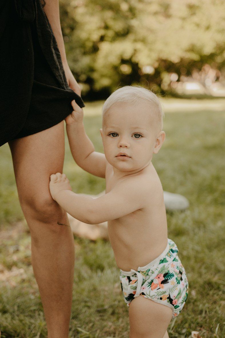 Baby steht auf Gras in einer Schwimmwindel mit tropischem Muster.