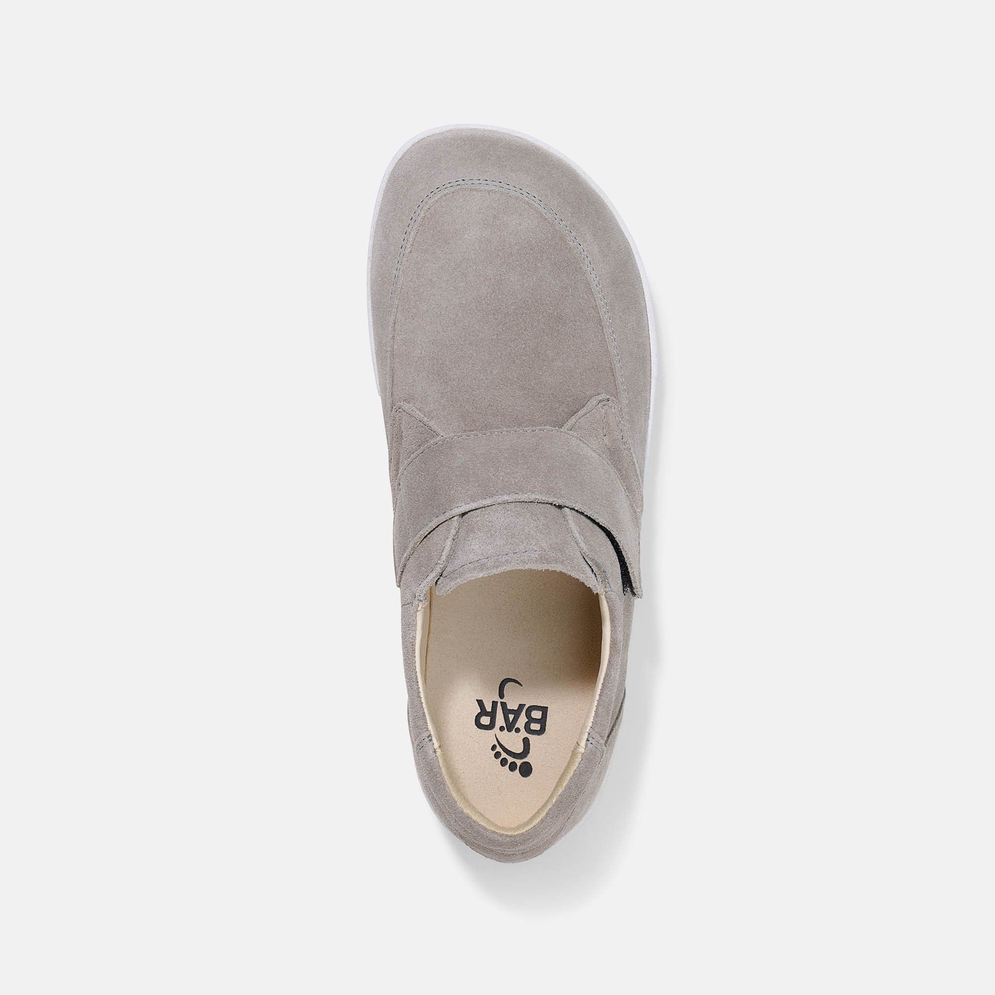 Draufsicht auf einen grauen Slipper mit Klettverschluss. Weiße Sohle. Innen steht BÄR. Obermaterial aus Wildleder.