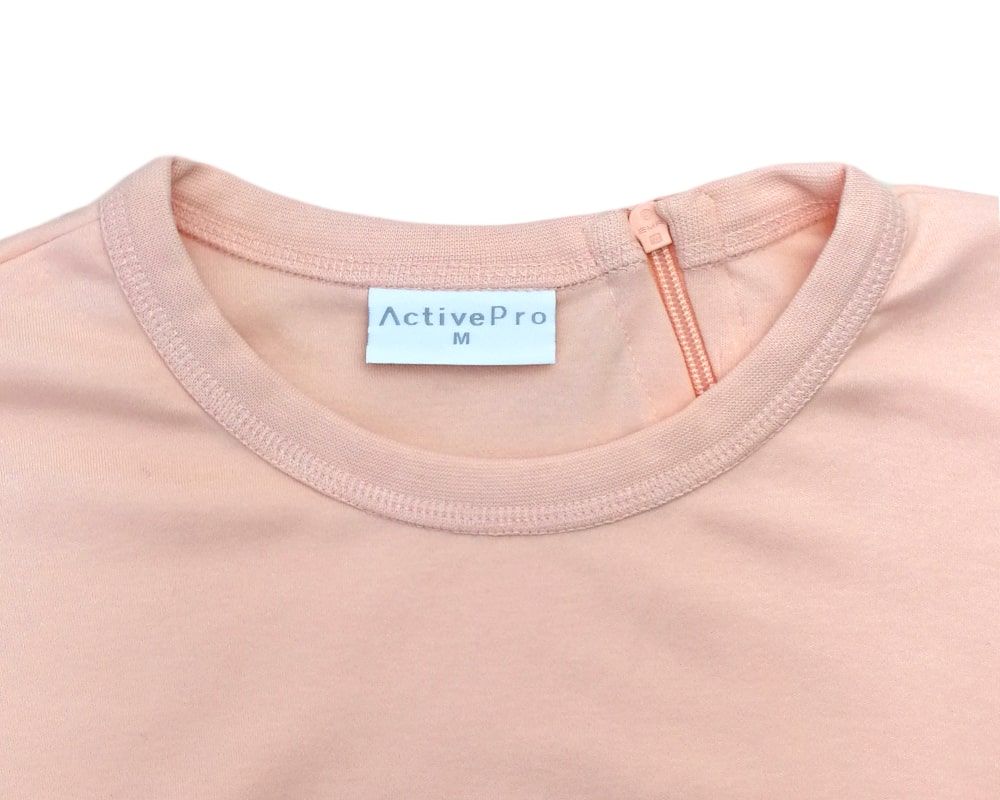 Detailansicht des aprikotfarbenen Pflegeoveralls. Etikett mit 'ActivePro' und Größe 'M' am Kragen.