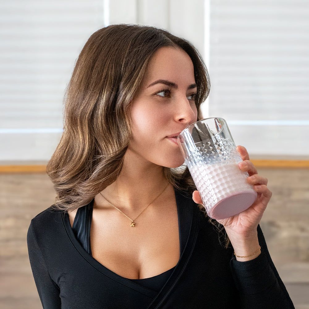 Frau trinkt aus einem Glas. Glas mit rosa Flüssigkeit. Frau trägt schwarzes Oberteil und Halskette.