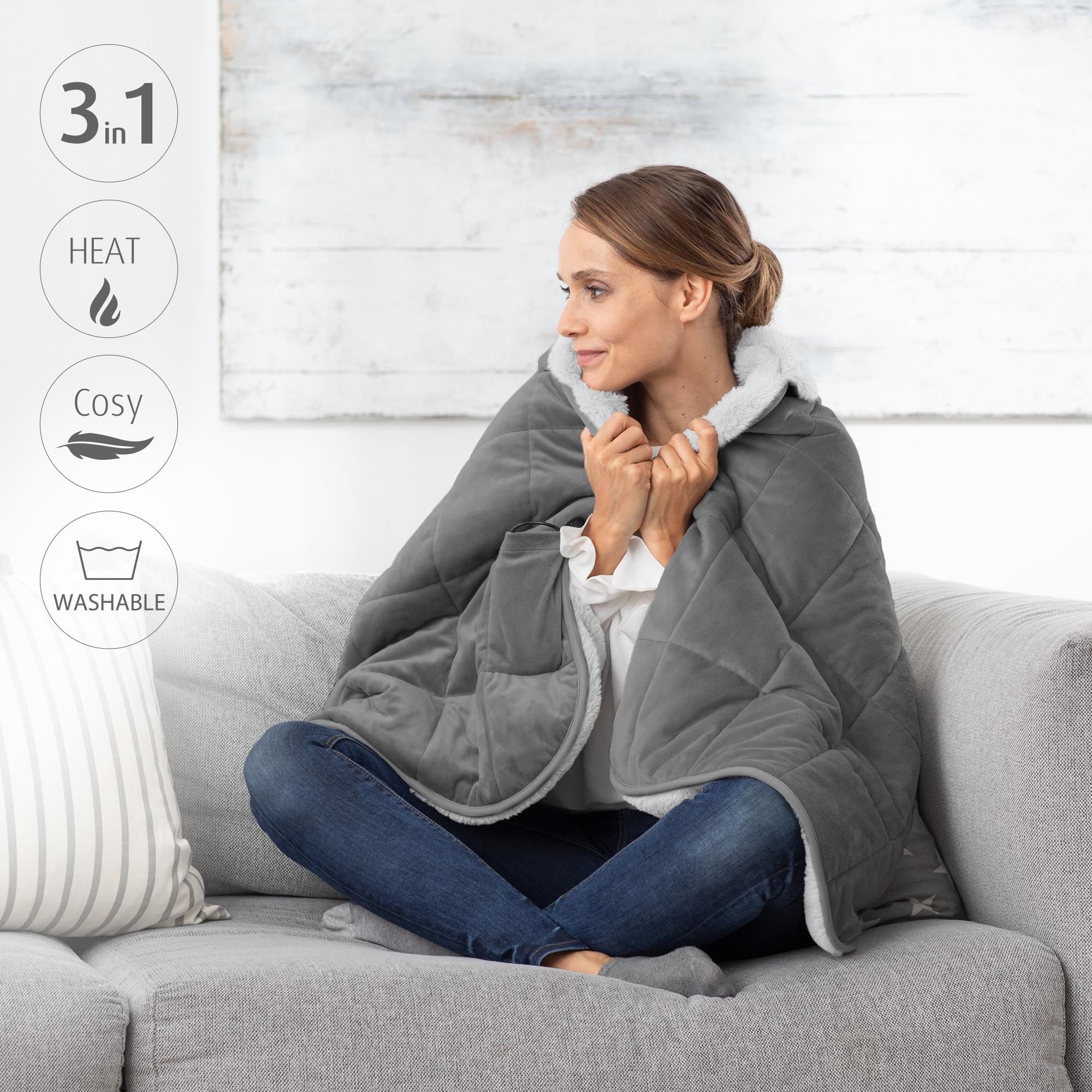 Frau sitzt auf Sofa, trägt graue Heizdecke. 3-in-1-Funktionen: Wärme, gemütlich, waschbar. Symbole.