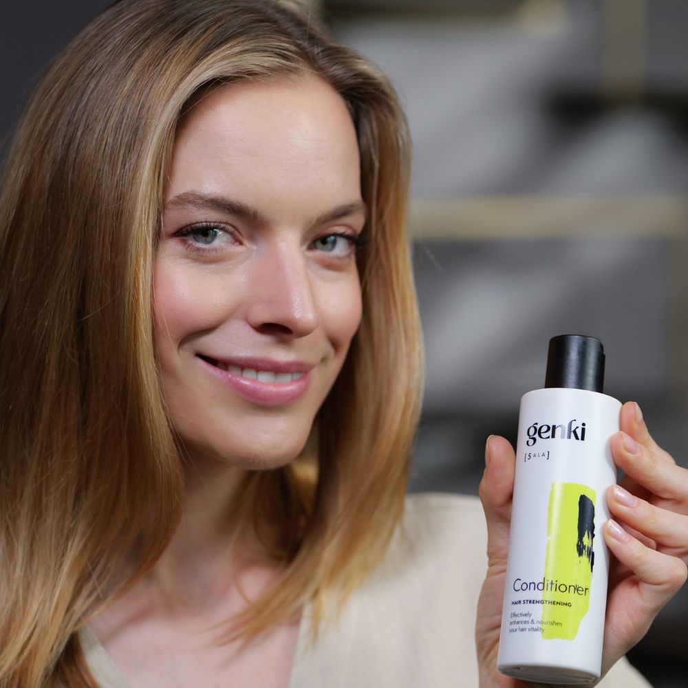 Frau hält Genki Conditioner-Flasche. Weiß mit schwarzem Deckel. Gelber Akzent. Lächelt.