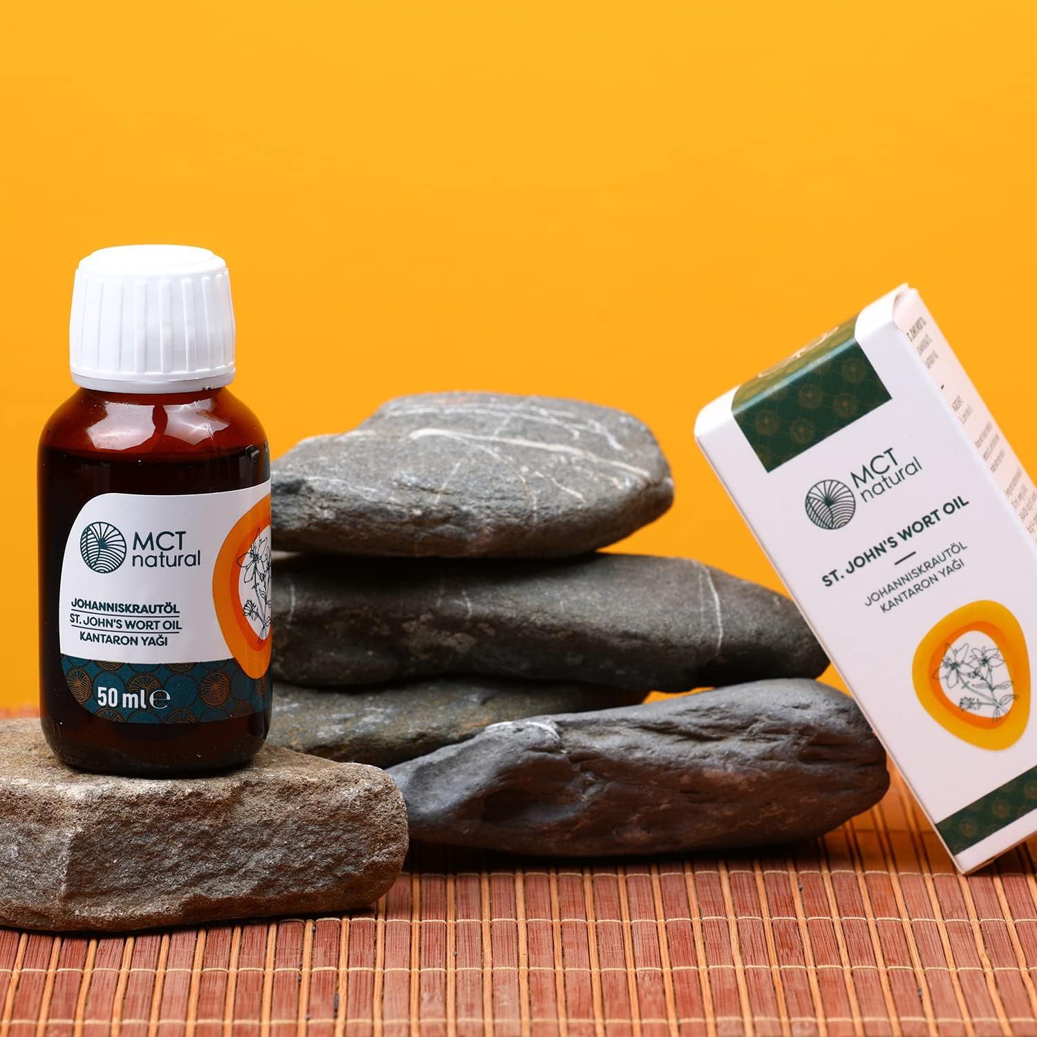 Braune Glasflasche mit weißem Deckel und Karton neben Steinen. Aufschrift: MCT natural, Johanniskrautöl. 50 ml.