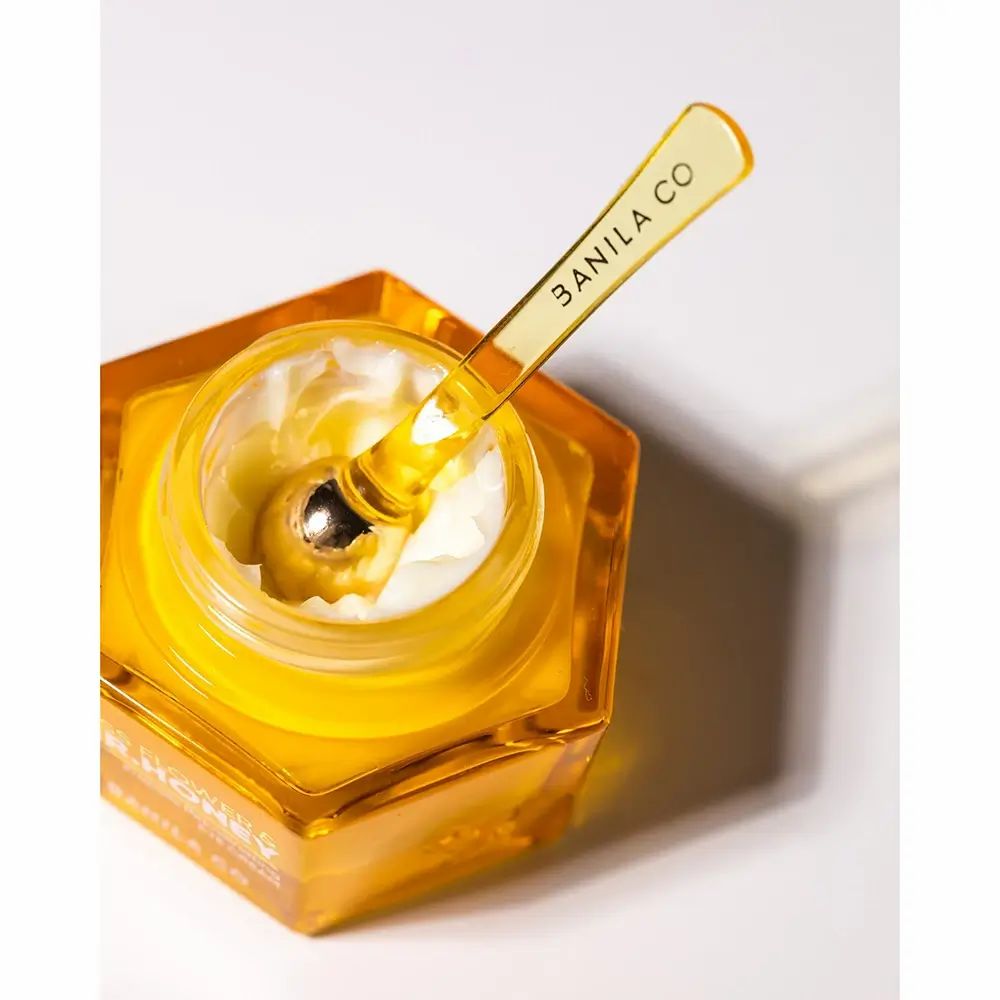 Tiegel mit Creme und Applikator. Applikator: BANILA CO, goldfarben, Löffelform. Creme sichtbar. Tiegel: MISS FLOWER & MR. HONEY.
