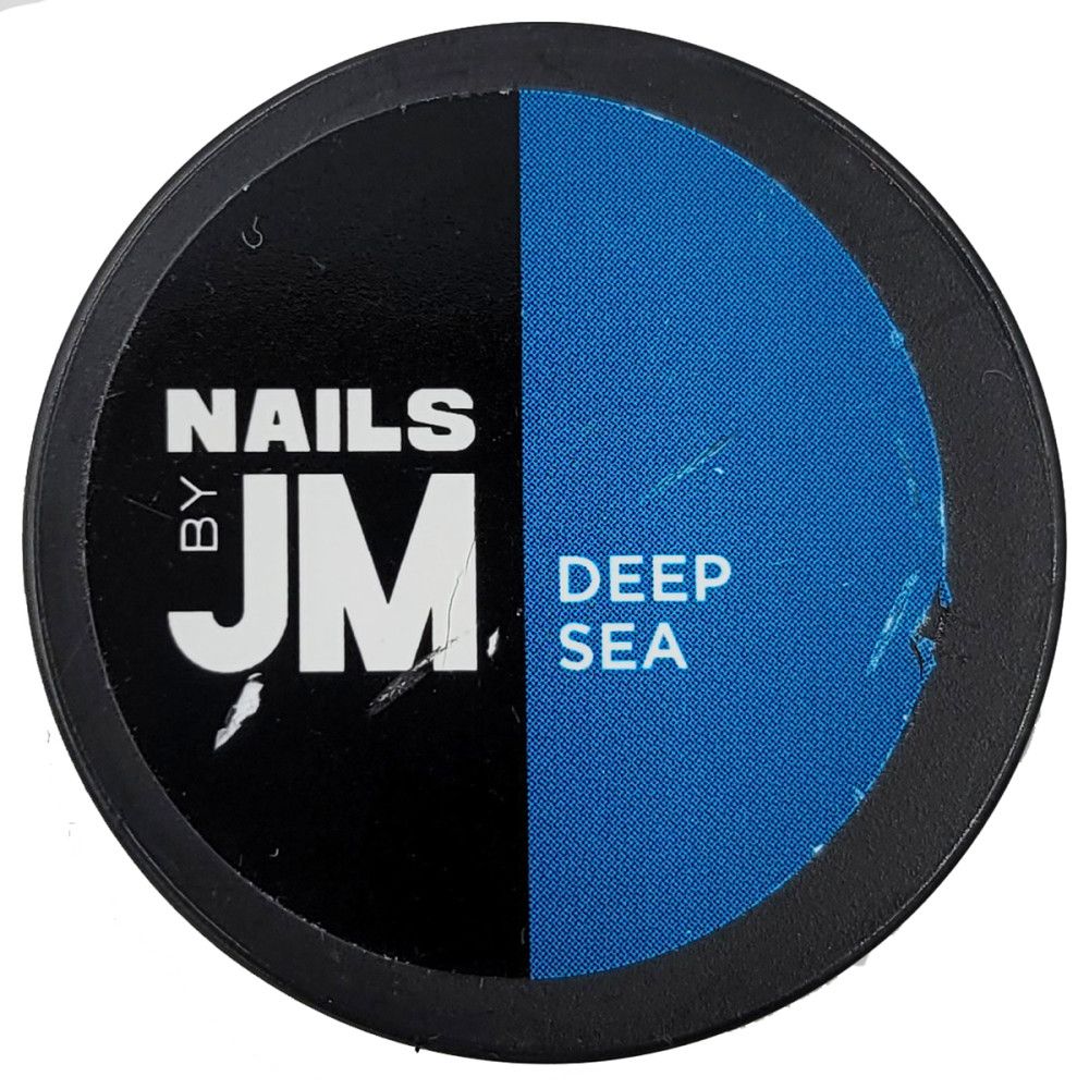Runder Behälter mit schwarzem und blauem Bereich. Aufschrift: NAILS BY JM, DEEP SEA. Kratzer auf der Oberfläche.