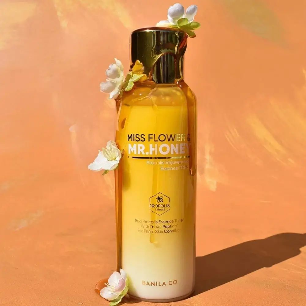 Gelb-weiße Flasche mit goldfarbenem Deckel. Aufschrift: Miss Flower & Mr. Honey. Mit Blüten dekoriert.