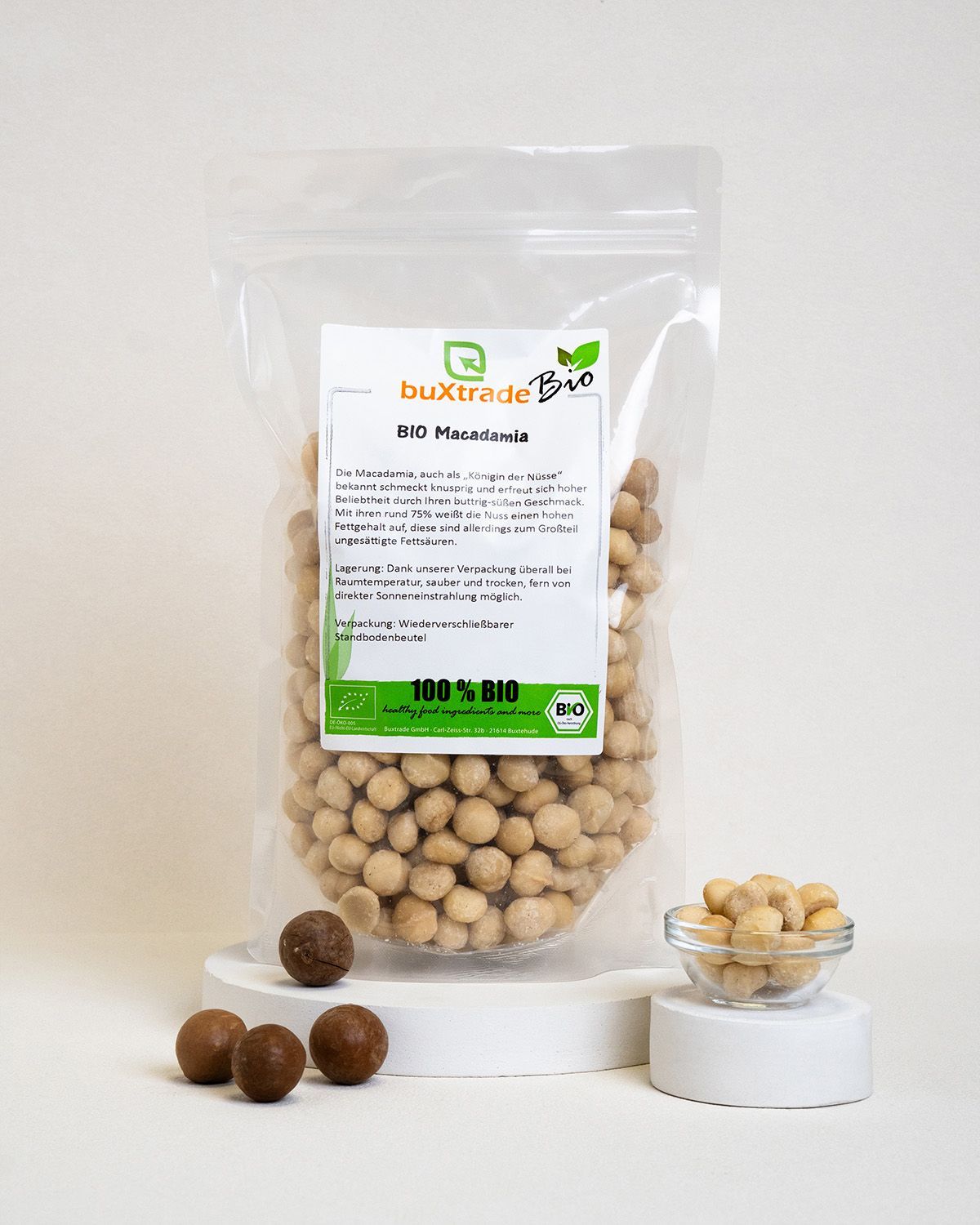 Transparente Verpackung mit BIO Macadamia-Nüssen, daneben eine Schale mit Nüssen und drei Nüsse.