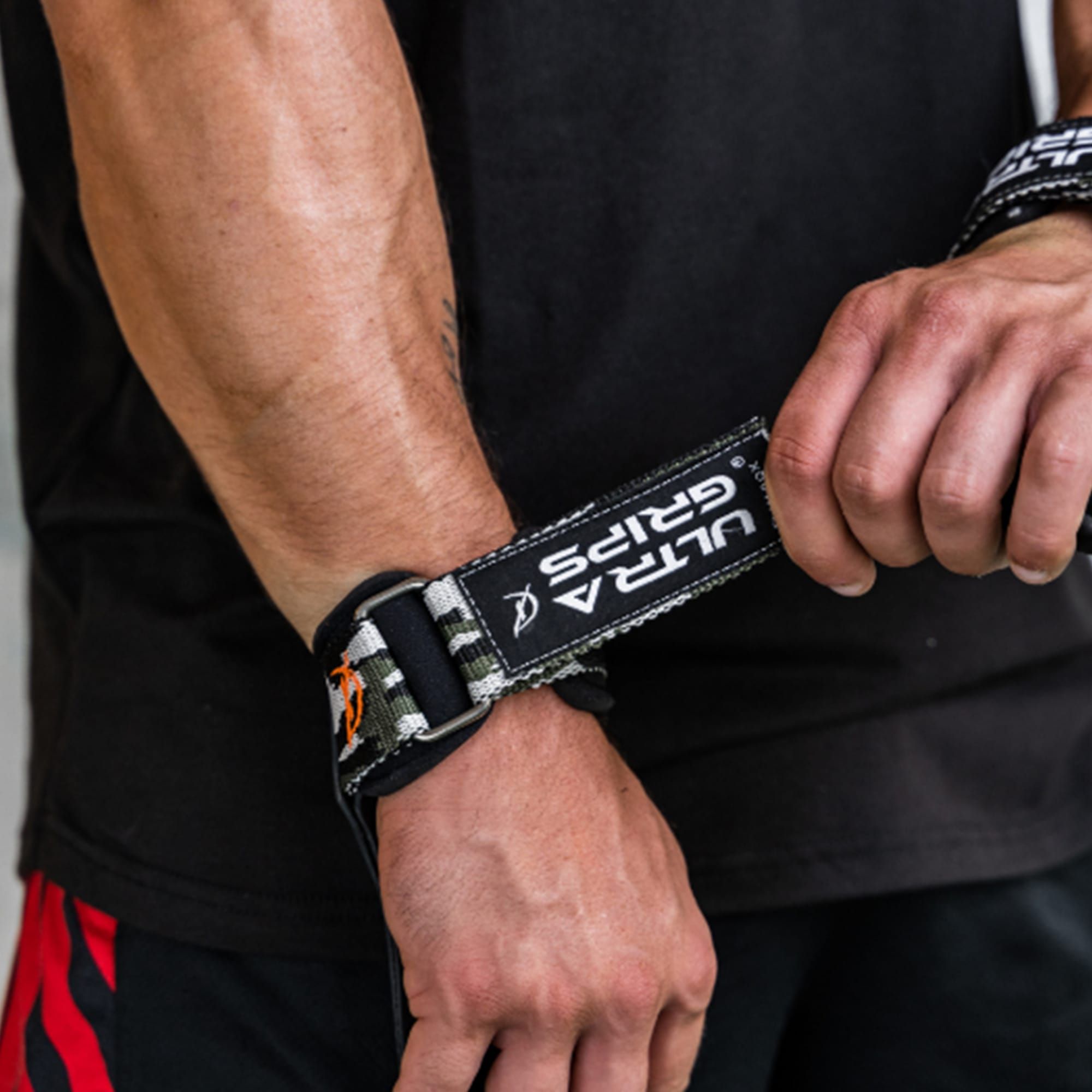 Person legt CLIMAQX Ultra-Grip an. Text: ULTRA GRIPS. Camouflage-Muster am Riemen. Schwarzes T-Shirt.