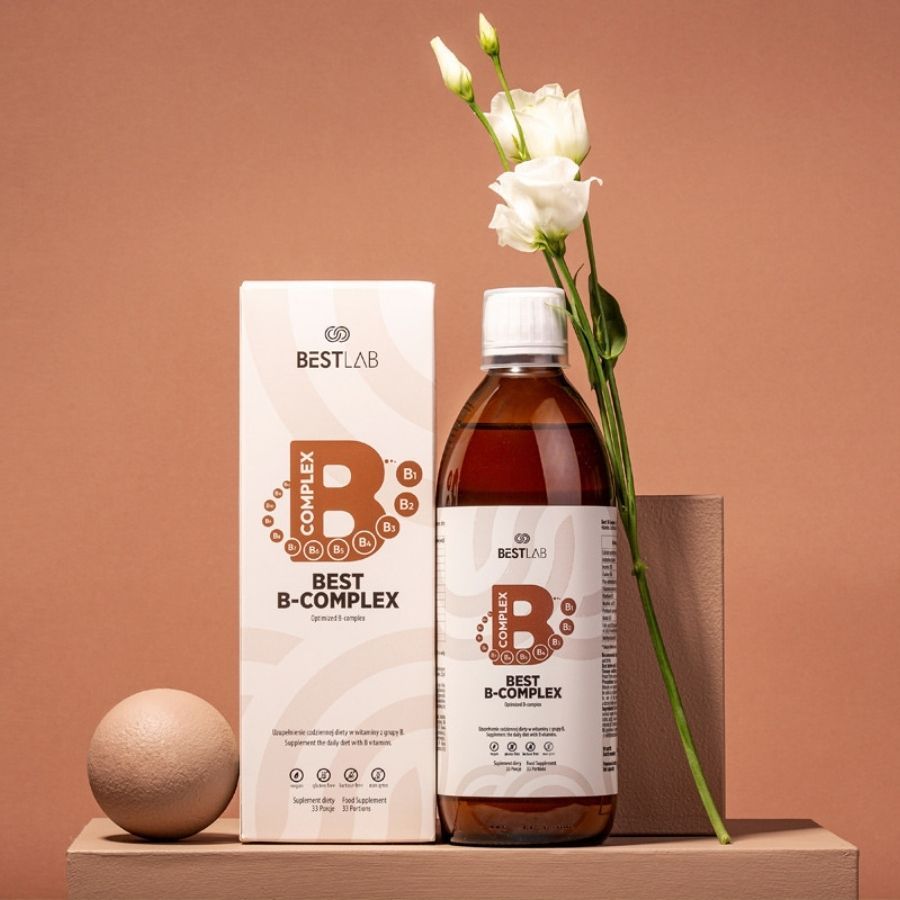 Braune Glasflasche und Karton "BEST LAB B-COMPLEX" auf Holzpodest. Weiße Blüten und Kugel als Dekoration.