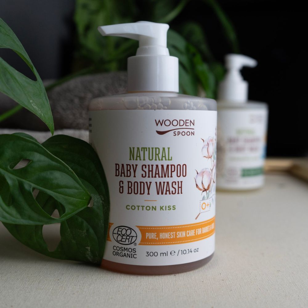 Flasche mit Spender. Aufschrift: NATURAL BABY SHAMPOO & BODY WASH, Cotton Kiss. Logo: COSMOS ORGANIC. 300 ml. Zweite Flasche im Hintergrund.
