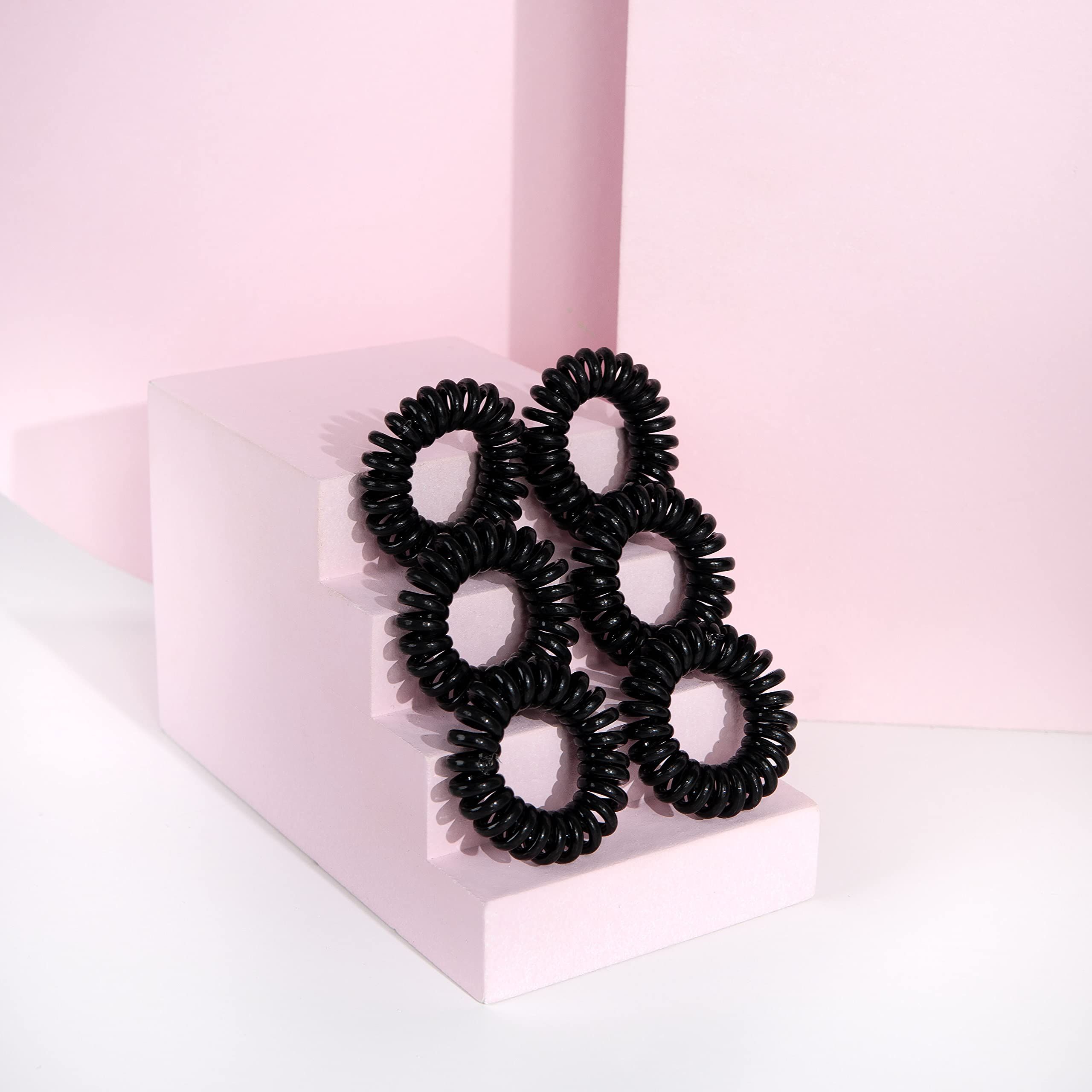 Mehrere schwarze, spiralförmige Haargummis auf einem rosa Podest. Rosa Hintergrund.