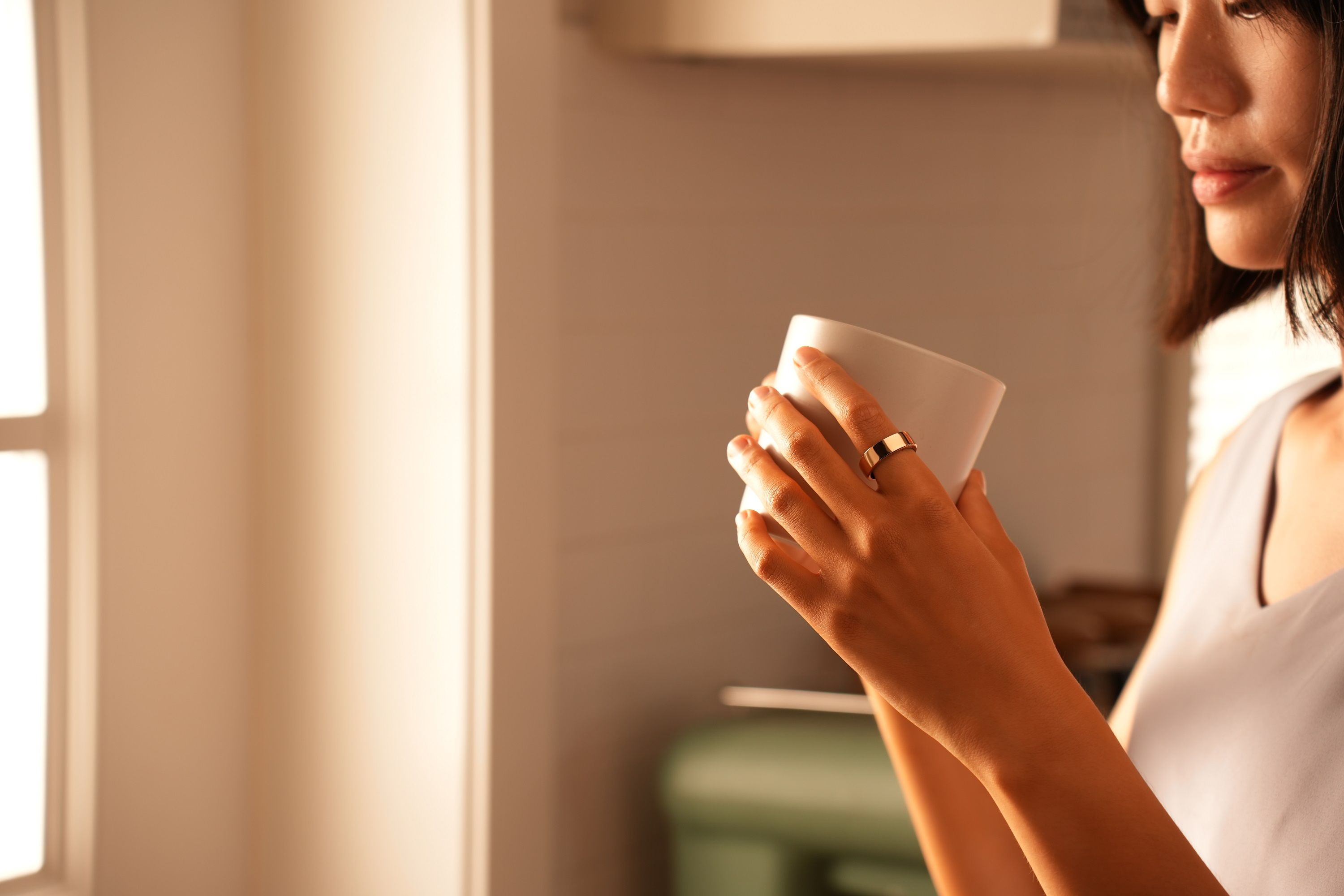Frau mit goldenem Ring, hält eine Tasse. Sie steht in einer Küche.