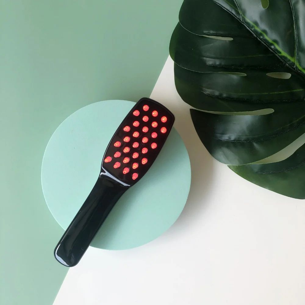 Schwarze Haarbürste mit vielen roten LEDs, auf einem mintgrünen Kreis liegend.
