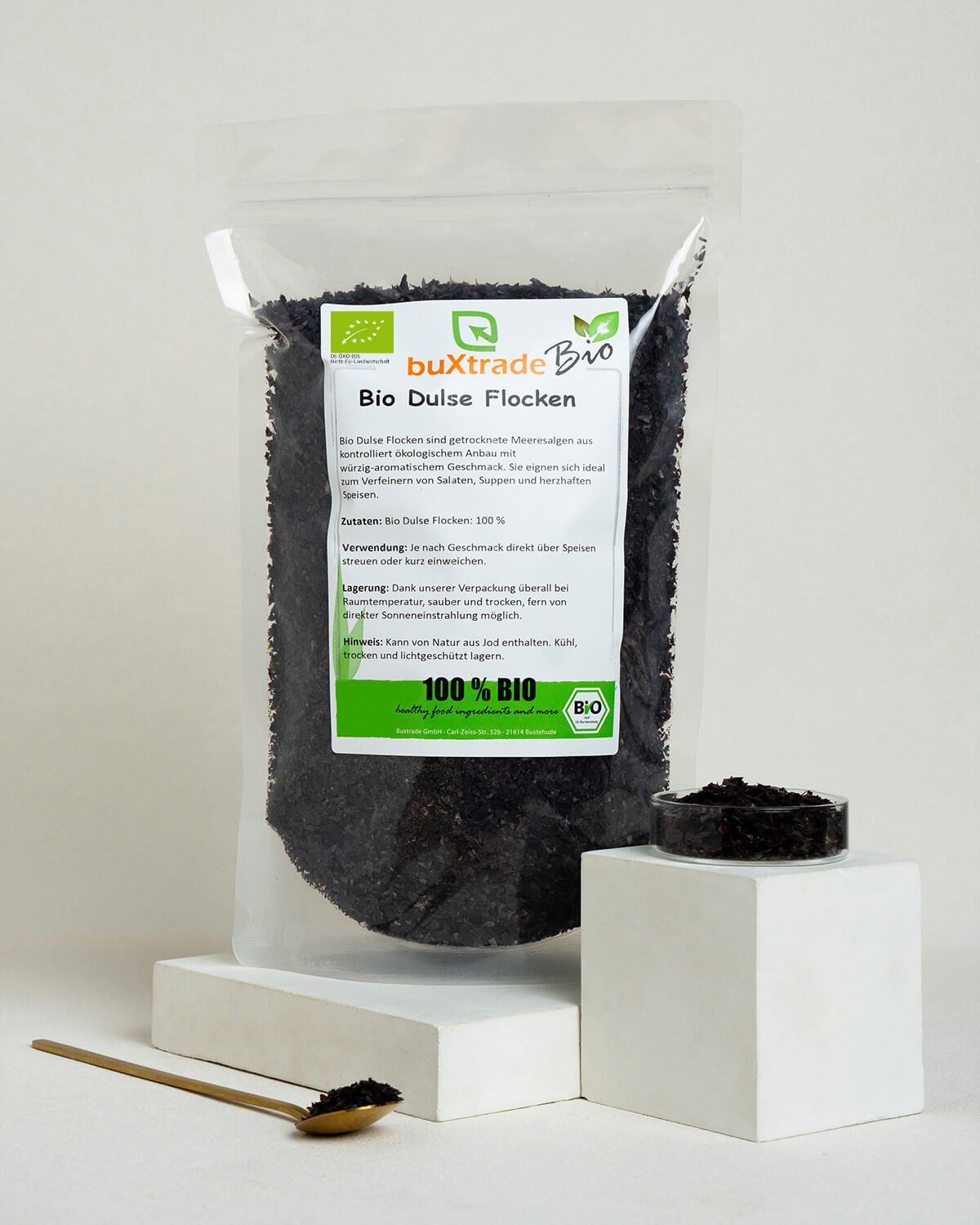 Buxtrade Bio Dulse Flocken, ein kleiner Behälter mit Flocken, Löffel mit Flocken.