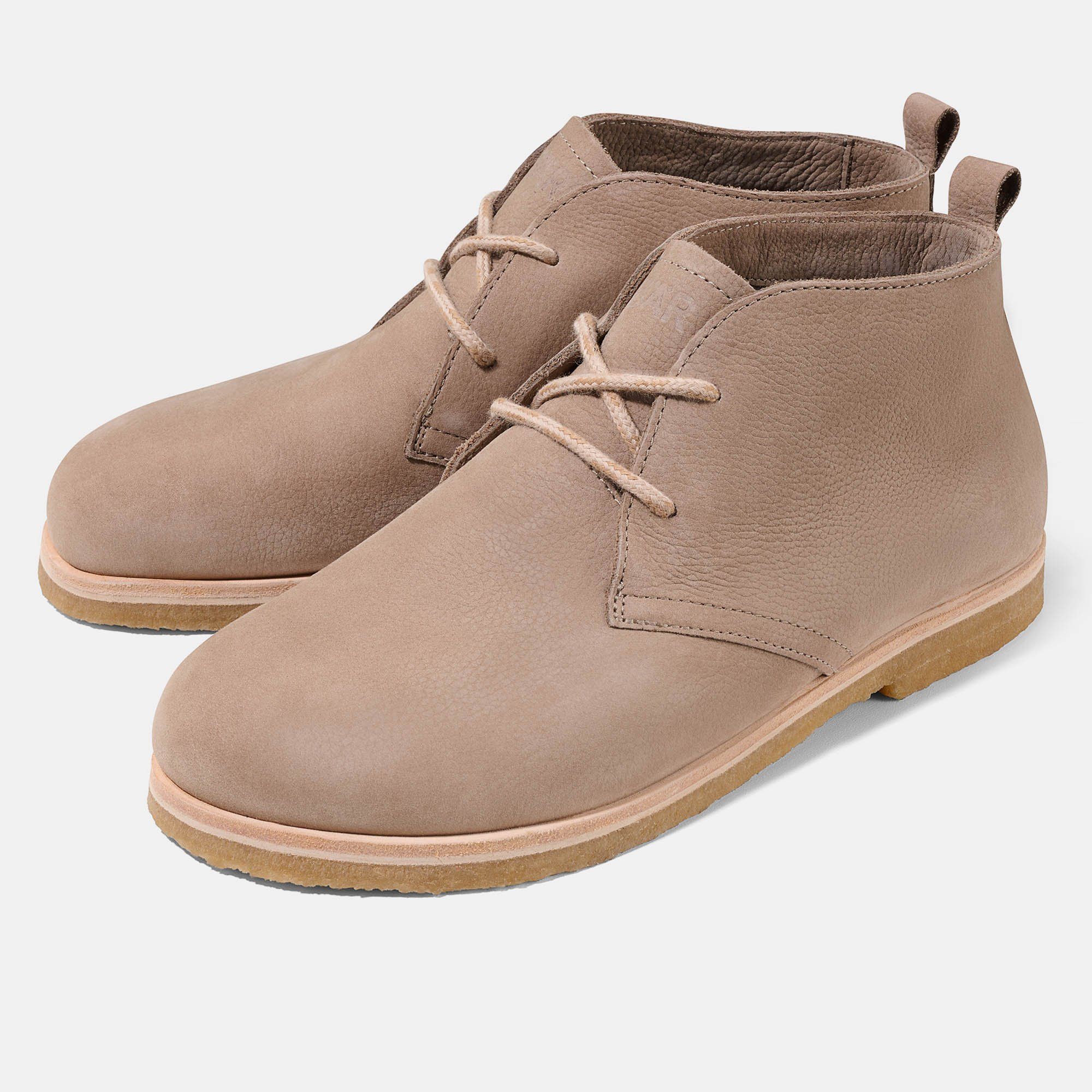 Zwei beigefarbene Stiefeletten mit Schnürsenkeln. Hellbraune Sohle. Obermaterial aus Leder. Auf hellem Hintergrund.
