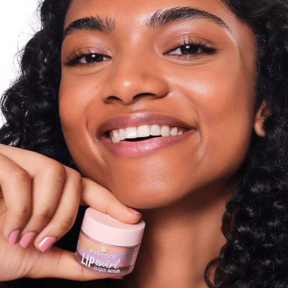 Person hält einen Tiegel mit Lippenpeeling. Aufschrift: essence LIP swirl sugar scrub. Person lächelt.