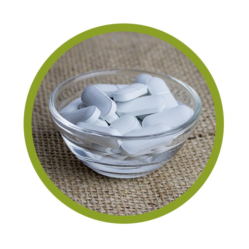 Klare Glasschale mit weißen Tabletten auf grobem Stoff.