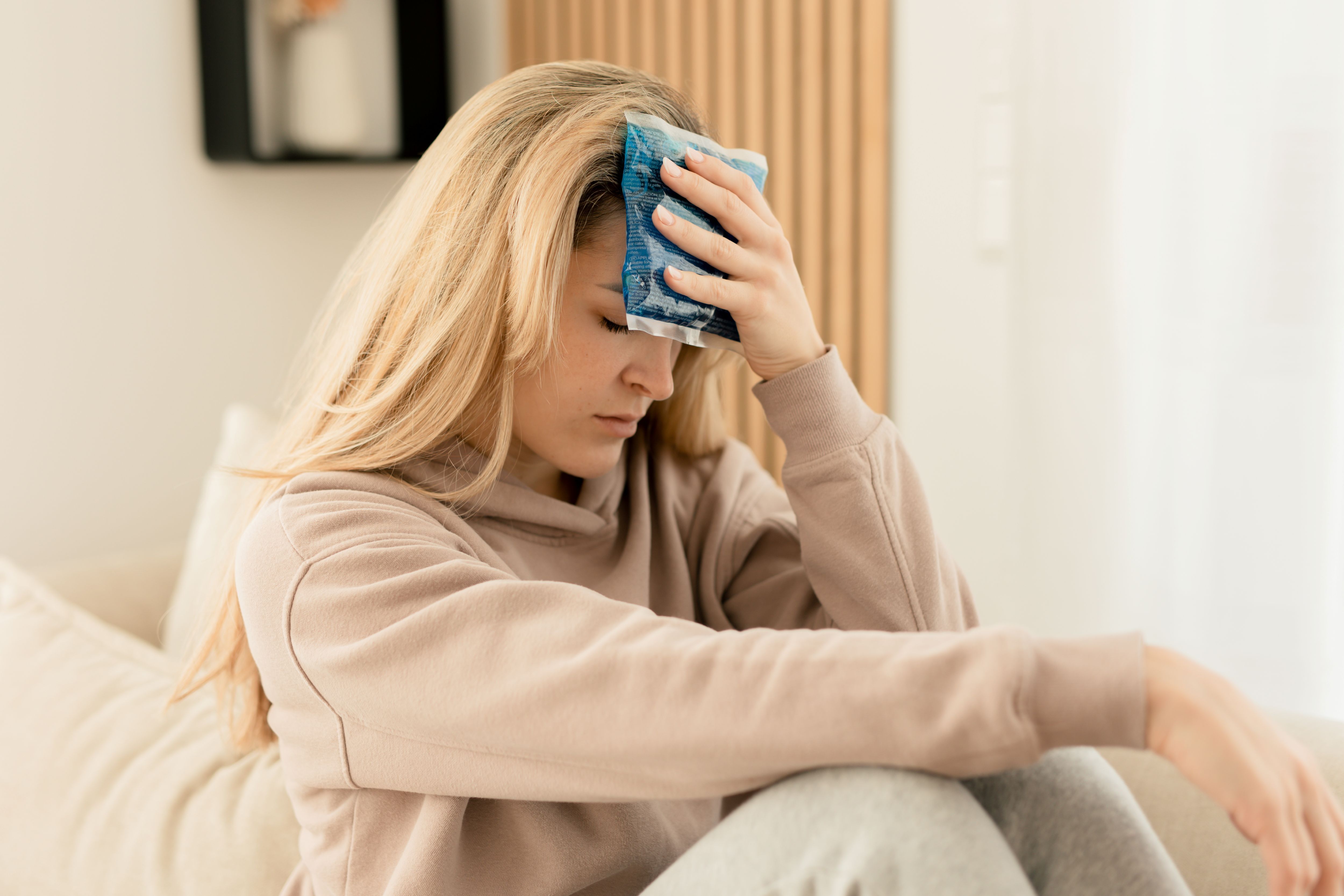 Una donna con una compressa caldo-fredda blu sulla fronte. È seduta su un divano.