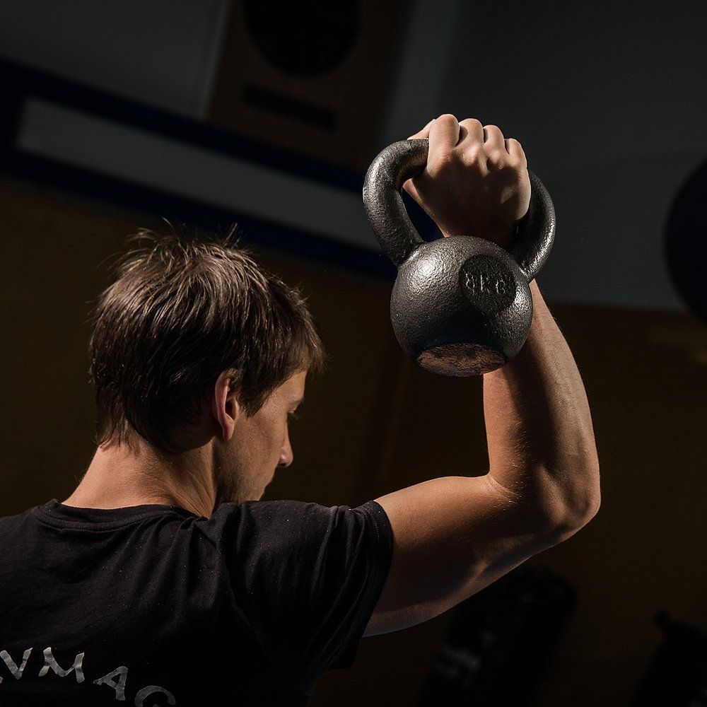 Person hebt eine lackierte, graue Kettlebell. Die Kettlebell ist mit 8 KG beschriftet. Der Griff ist oben.