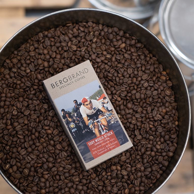 Kaffeebohnen in Metallbehälter. Packung mit Eddy World Attack-Etikett liegt in den Bohnen.