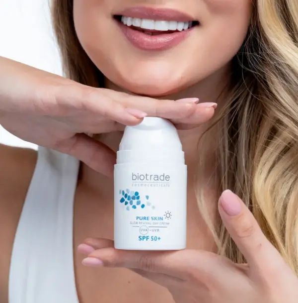 Frau hält eine weiße Creme-Flasche. Aufschrift: Biotrade, Pure Skin Glow Revival Day Cream SPF 50+.